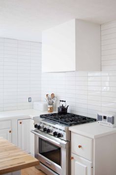 a stove top oven sitting inside of a kitchen next to a wooden table and white cabinets