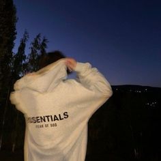 a person wearing a white sweatshirt with the words essentials printed on it, covering their face