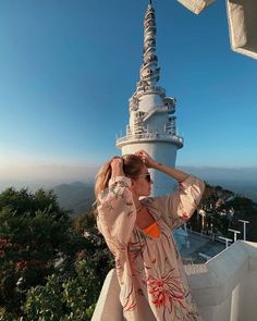 a woman standing on top of a tall tower next to a lush green hillside under a blue sky