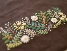 embroidered flowers and leaves on brown fabric with white stitching in the center, closeup