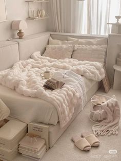 a white bed sitting in a bedroom next to a window with lots of pillows on top of it