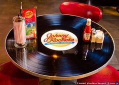 a table topped with a vinyl record next to a shaker and two bottles of soda