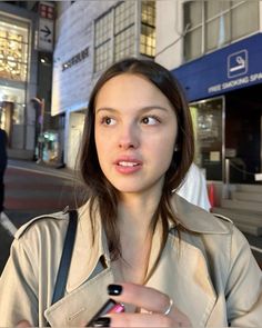 a woman standing in front of a building holding a cell phone and looking at the camera