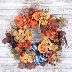 a wreath with orange and yellow flowers hanging on a white wooden wall next to black berries