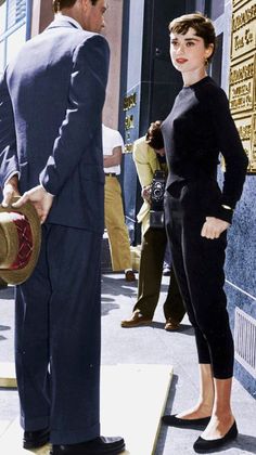 a man in a suit and tie standing next to a woman with a hat on her head