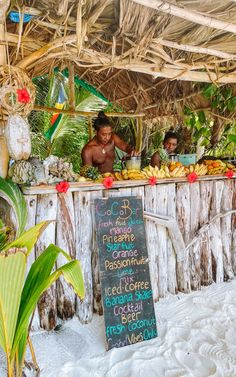 a man standing behind a table filled with food under a thatch roofed roof over looking the ocean