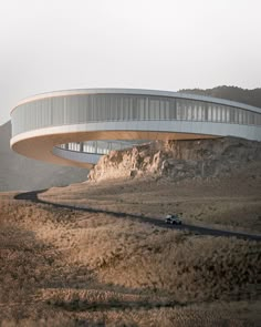 a car is driving on the road near a large circular building in the middle of nowhere