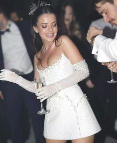 a woman in a short white dress holding a wine glass and wearing a tiara