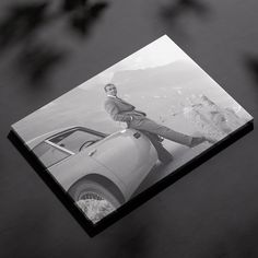 a black and white photo of a woman leaning on a car