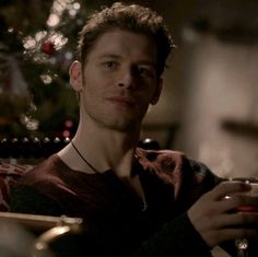 a man sitting at a table with a glass in his hand and a christmas tree in the background