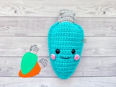 a crocheted blue peal with a carrot shaped object next to it on a white wooden background