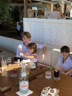 three young children sitting at a table with drinks and food on the table in front of them