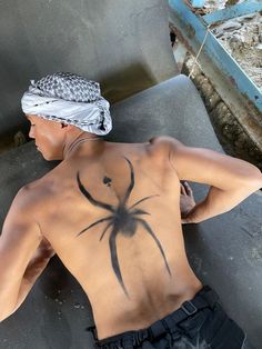 a man with a spider tattoo on his back sitting in front of a metal structure