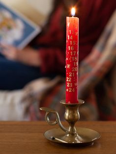 a lit candle sitting on top of a wooden table next to a woman reading a book