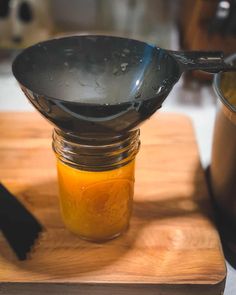 a wooden cutting board topped with a glass jar filled with liquid and a metal spoon