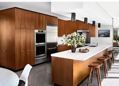 a modern kitchen with wooden cabinets and white counter tops, along with bar stools