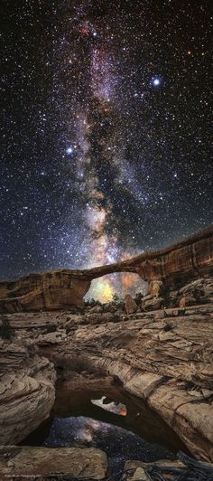 the night sky with stars above rocks and an arch in the foreground, as seen from below