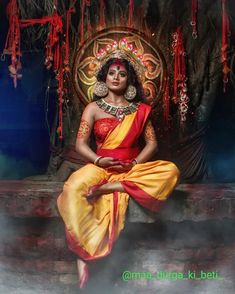 a woman in a red and yellow dress sitting on a stone wall with an elaborate headpiece