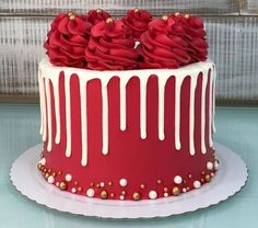 a red cake with white icing and roses on top is sitting on a plate