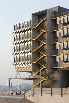 a tall building with stairs going up to it's top level and people walking on the sidewalk below