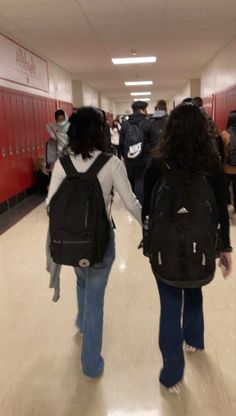 two people walking down a hallway with backpacks