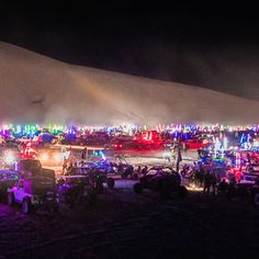 many cars are parked in the parking lot at night with colorful lights on them and people standing around