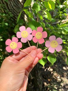 a hand holding pink flowers with smiley faces on them