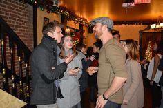 a group of people standing around each other in a room with christmas lights on the walls