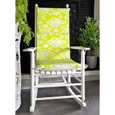 a white rocking chair with a yellow and white patterned seat cover next to a potted plant