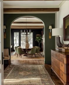 a dining room with green walls and wooden floors, an archway leading to the living room