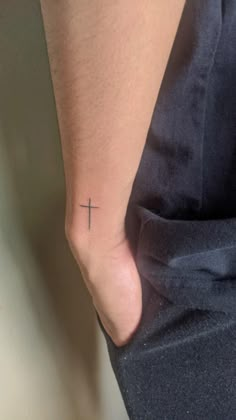 a person with a cross tattoo on their left foot, standing next to a wall