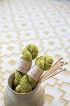 three skeins of green yarn in a vase on a tableclothed surface