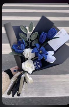 a bouquet of blue and white flowers in a black box on the street with someone's hand holding it