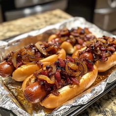 three hotdogs with onions and bacon on tin foil lined up on a counter