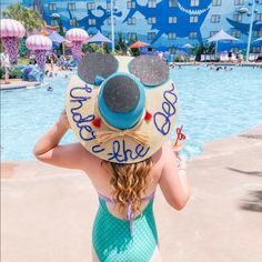 a woman wearing a mickey mouse hat in front of a pool at disney's beach resort