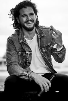 a man with long hair and beard sitting on top of a skateboard wearing a jean jacket