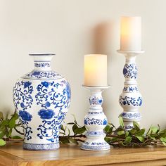 three blue and white vases sitting on top of a wooden table next to candles