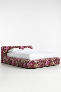 an upholstered bed with white sheets and pink flowers