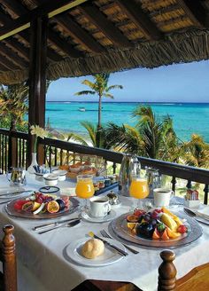 an outdoor dining area overlooking the ocean with fruit, juice and coffee on the table