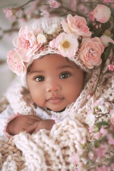 Adorable baby girl with big brown eyes wearing a floral headband and wrapped in a soft, textured blanket surrounded by pink flowers. Unique Names For Girls