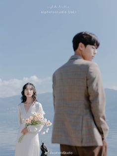 a man and woman standing next to each other in front of a body of water