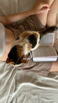 a woman laying on top of a bed next to an open book and a cat