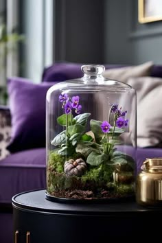 a glass clochet with purple flowers in it on a table next to a couch