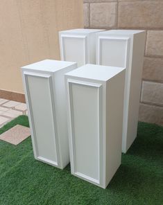 three white cabinets sitting on top of a green grass covered floor next to a building