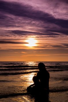 a woman sitting on the beach at sunset