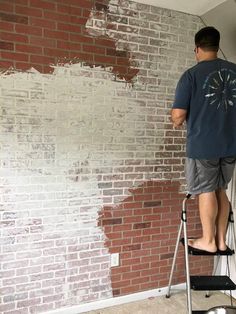 a man standing on a step ladder painting a brick wall