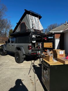 a truck with a tent on the back parked in front of a house next to boxes