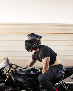 a man riding on the back of a motorcycle wearing a black helmet and holding onto his bike