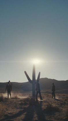 three people are walking in the desert near a cactus and a large saguado