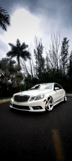 a white car is parked on the side of the road in front of some palm trees